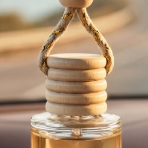Clear glass car diffuser with a natural wood cap hanging in a sunlit car interior with a scenic road background.