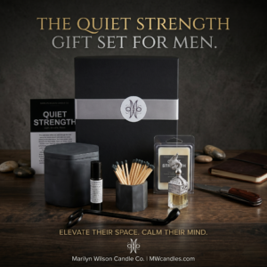 The Quiet Strength Gift Set for Men by Marilyn Wilson Candle Co. displayed on a dark walnut wood surface against a moody charcoal background. The collection includes a premium black gift box with silver ribbon and white monogram seal, an 11 oz handcrafted charcoal concrete hexagon candle, a Quiet Strength wax melt clamshell, a Pocket Reset roll-on bottle, a concrete hexagon match holder filled with long wooden matches with dark tips, a glass car diffuser, and a matte black wick trimmer. The Quiet Strength gift card leans against the box. Gold text at the top reads The Quiet Strength Gift Set for Men. Gold text at the bottom reads Elevate Their Space. Calm Their Mind. Marilyn Wilson Candle Co. MWcandles.com.